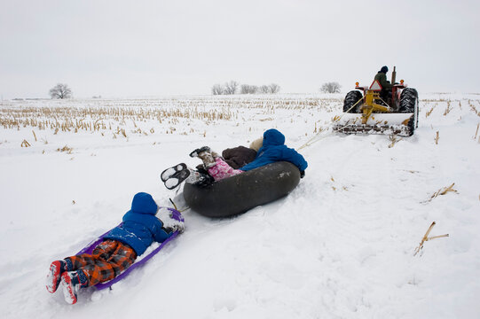 Children ride sleds behind a tractor on a farm near Cortland, Nebraska, USA; Cortland, Nebraska, United States of America