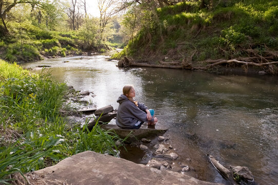 Teenage girl relaxes along a stream; Dunbar, Nebraska, United States of America