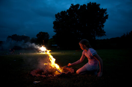 Teenage girl stokes a campfire in a park at night on the fourth of July; Lincoln, Nebraska, United States of America