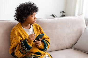 African girl holding smartphone touch screen typing scroll page at home. Woman with cell phone surfing internet using social media apps playing game. Shopping online Internet news cellphone addiction