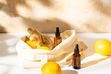 Sunlit scene of brown glass cosmetic serum bottles with lemon and ginger in a cotton canvas tote bag on bright earthy background. Fresh and healthy fruit arrangment.