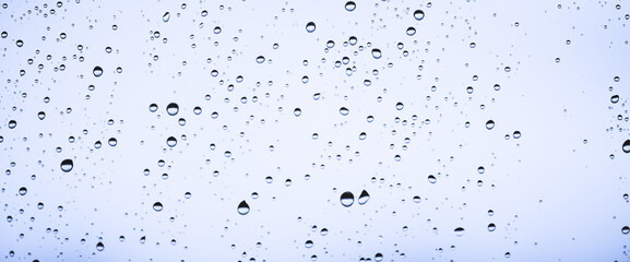 Minimal light backdrop with rain droplets on white glass. Light wet window with rainy drops closeup in blue light. Blurry minimalist monochrome background of window glass with raindrops close up.