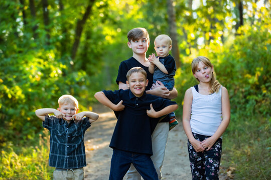 Outdoor portrait of five young siblings making funny faces while standing on a trail in a woodland; Edmonton, Alberta, Canada