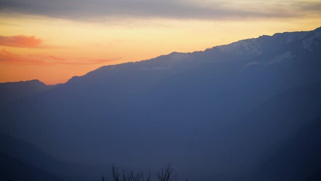 panning shot showing beautiful sunset colors in hampta village kullu manali with mighty himalaya mountains lost in fog