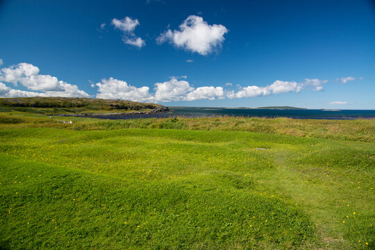 Outline and mounds in the grass containing an ancient Viking building site; L'Anse aux Meadows, Newfoundland and Labrador, Canada