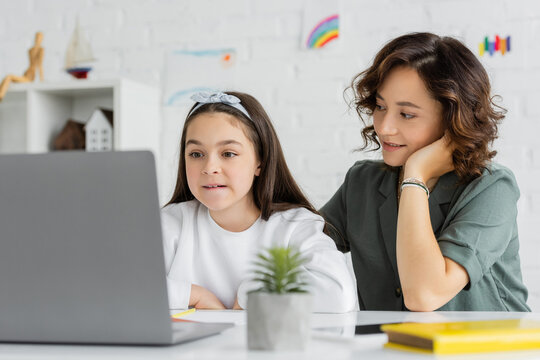 Smiling mother looking at child talking during speech therapy video call on laptop at home. - Powered by Adobe