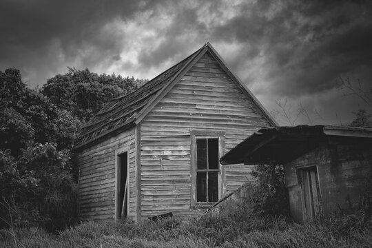 Black and white image of a spooky old abandoned house under threatening weather clouds in Eastern Washington, USA; Colfax, Washington, United States of America
