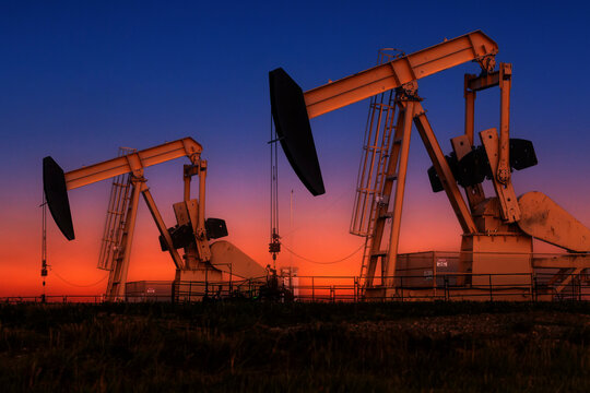 Glowing colourful pumpjacks at sunrise with glowing sky in the background, West of Airdrie; Alberta, Canada