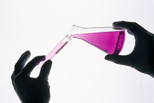 Studio shot of a gloved hand chemical being poured into a glass tube;  New York City, New York, United States of America