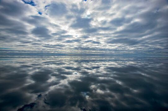 Mirror image of a cloudy sky reflected on the surface of ocean water; Svalbard Archipelago, Norway