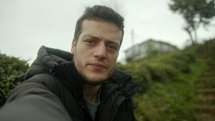 A Handsome Young Brown-Haired Man in a Black Jacket Conducts a Video Conference Against a Beautiful Nature House Background - POV Shot