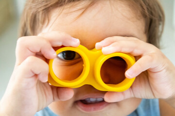 Baby looking through a yellow plastic toy positioned over her eyes and being held by her little hands. Mention of brain development and neurological deficits in childhood with their treatment.