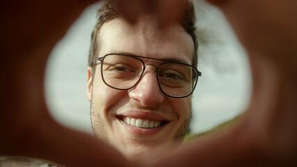 The concept of health - Beautiful tall, handsome young doctor with brown hair and glasses, forms a heart with his hands, looking at the camera with a warm smile