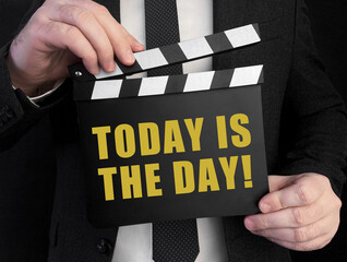 Obraz premium A businessman holds up a ?lapperboard with text Today Is The Day!