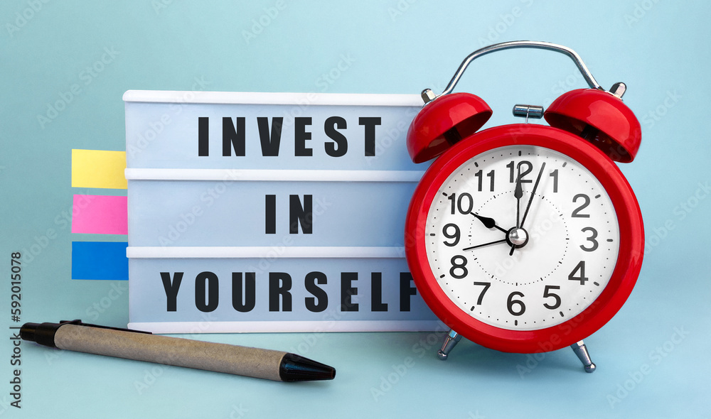 Poster text invest in yourself written on the lightbox with alarm clock and colorfull stickers on blue back
