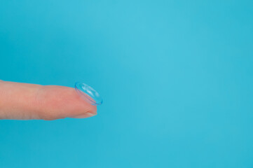 Woman holding contact lens on blue background. 