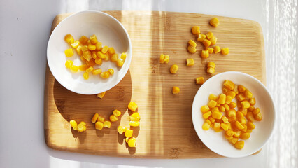 Lot of pieces of canned yellow corn on plate which is on wooden bamboo cutting board on white background. The concept of cooking and delicious healthy food