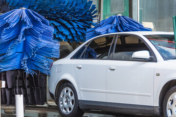 Automatic wash blue brush in action, white car comes out ready clean.