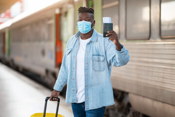 Fototapeta na wymiar Black Man Wearing Medical Face Mask Standing Near Train At Railway Station