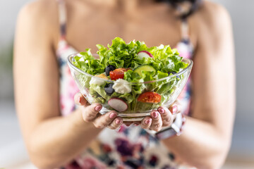 A young woman is holding a healthy spring salad in a glass bowl