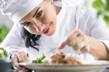 A young female chef finishes the meal with herbs in the restaurant kitchen - Close up