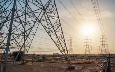 Large tall steel power pylons in rather flat landscape of Saudi Arabia, only black silhouettes...