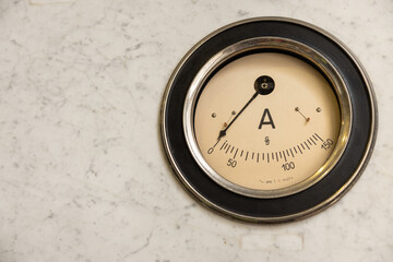 Vintage metal-rimmed round ammeter attached to a marble wall
