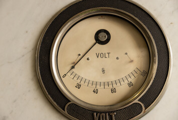 An antique non-functioning voltmeter in a round frame hangs on the wall