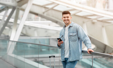 Happy Tourist Guy Texting On Cellphone Standing In Modern Airport