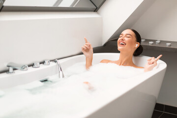 Woman Taking Bath Enjoying Relaxing Playlist Wearing Earbuds In Bathroom