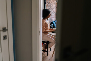 Remote side view of curly African female student typing on notebook keyboard studying working online. Black businesswoman working on laptop at desk. Afro lady working remotely from home office.