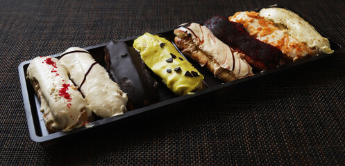 Classic French eclairs of oblong shape with various fillings and chocolate, mango, fruit creams on them. Close-up