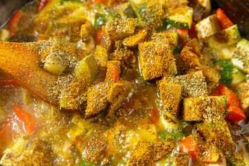 Obraz na płótnie Canvas Frying pan with stewed vegetables in sauce and spices with a wooden spoon close-up.