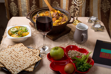 A set table for the Passover Seder with traditional matzah, wine, maror and a hot cholent for the meal and menorah.