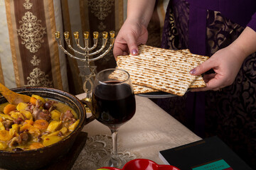 A woman at the table laid for the Passover seder holds matzah in her hands.