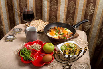 A set table for the Passover seder with traditional paraphernalia for the ritual and shakshuka in a frying pan.