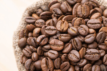 Dark roasted coffee beans in linen sack against wooden background. Fresh aromatic coffee grain