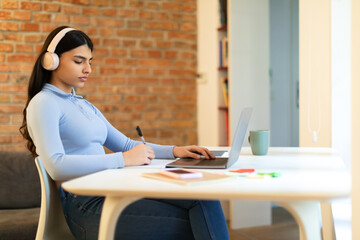Distance learning concept. Teenager lady studying with laptop, taking notes and doing homework...