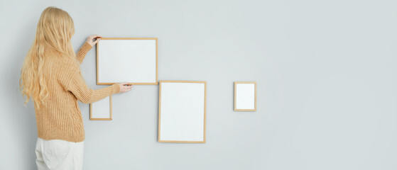 Blonde woman hanging blank photo frames on light wall
