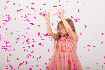 Obraz na płótnie Canvas little girl blonde in a pink dress catches confeti smiling happy on white background, holiday concept. A child is celebrating a birthday on a white background
