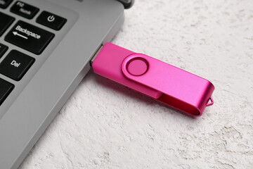 Laptop with pink USB flash drive on light background, closeup