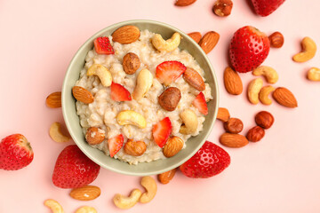 Bowl with tasty oatmeal, almonds, strawberries and hazelnuts on pink background