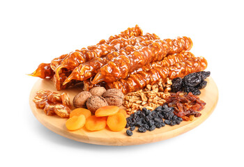 Wooden board with tasty churchkhela, walnuts and dried fruits on white background