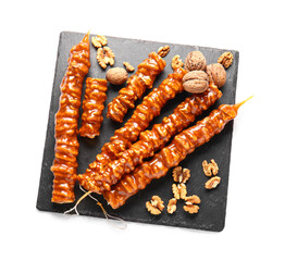 Slate board with tasty churchkhela and walnuts on white background