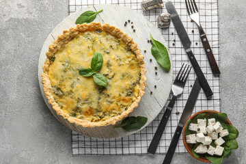 Board with delicious quiche and cutlery on grey grunge background