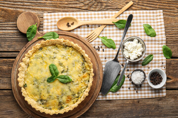 Fototapeta na wymiar Board with delicious quiche and spinach leaves on wooden background