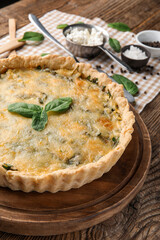Board with delicious quiche and spinach leaves on brown wooden background