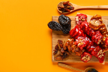 Board with delicious churchkhela and ingredients on orange background