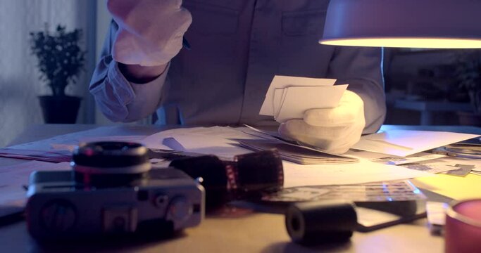The detective's hands accumulate information at the table. He hand writes text on paper, evidence. White gloves protect hands from fingerprints.