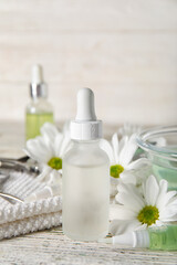 Bottle of cuticle oil and chamomile flowers on light wooden table, closeup